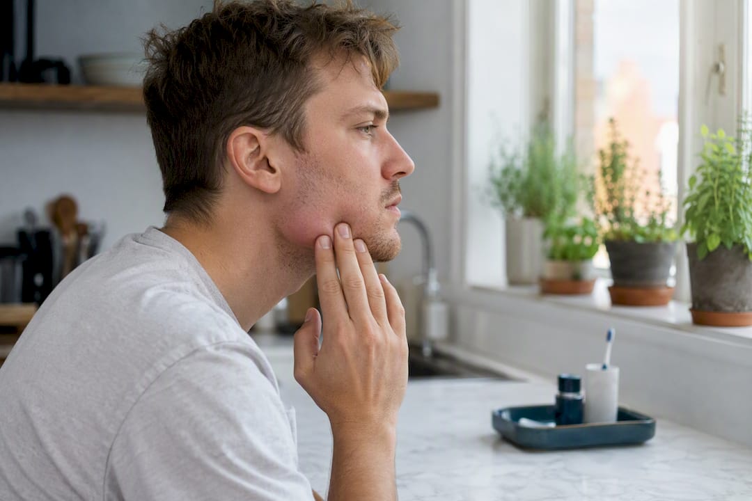 Person inspecting swollen jaw area in mirror