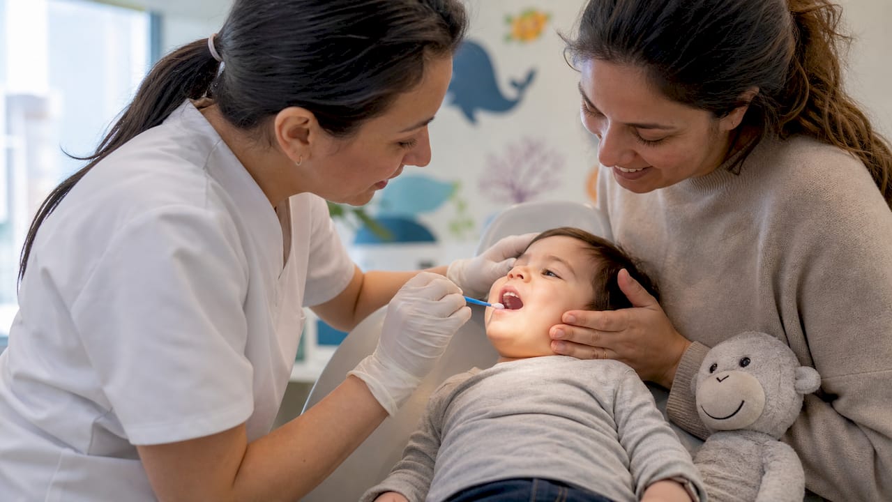Pediatric dentist applying fluoride varnish with parent nearby