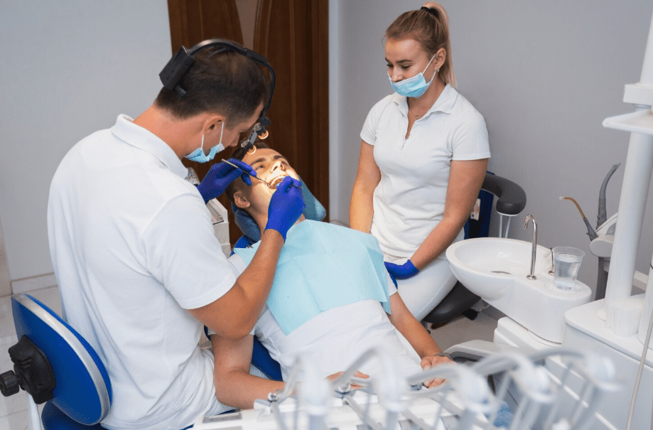 An emergency dental service being performed by a male dentist wearing a headlamp and blue gloves while a dental assistant looks on.